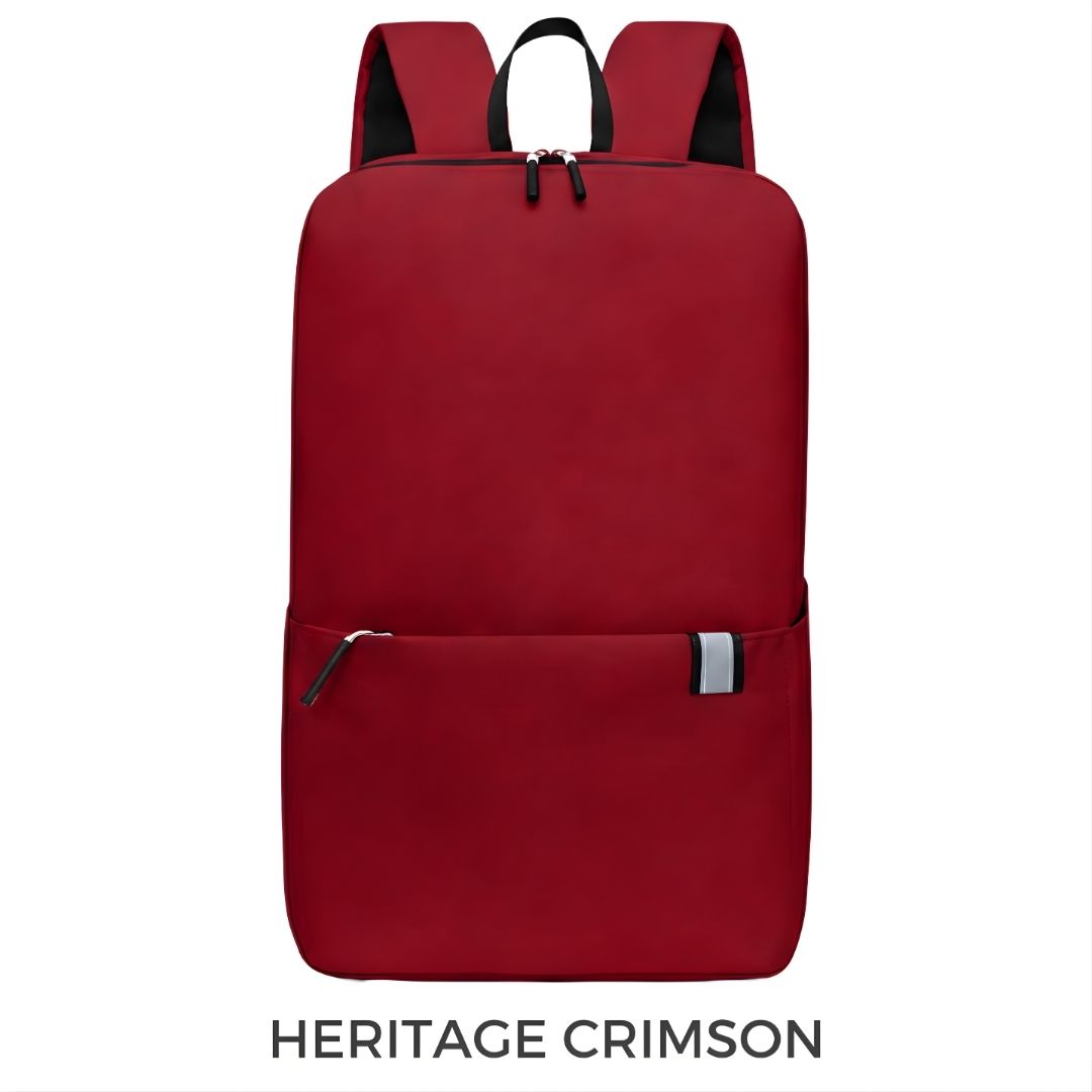 A red backpack shown from the front on a white background, with the text 'HERITAGE CRIMSON' underneath. The backpack has black shoulder straps, a black top handle, and a front zippered pocket with a small silver reflective accent.