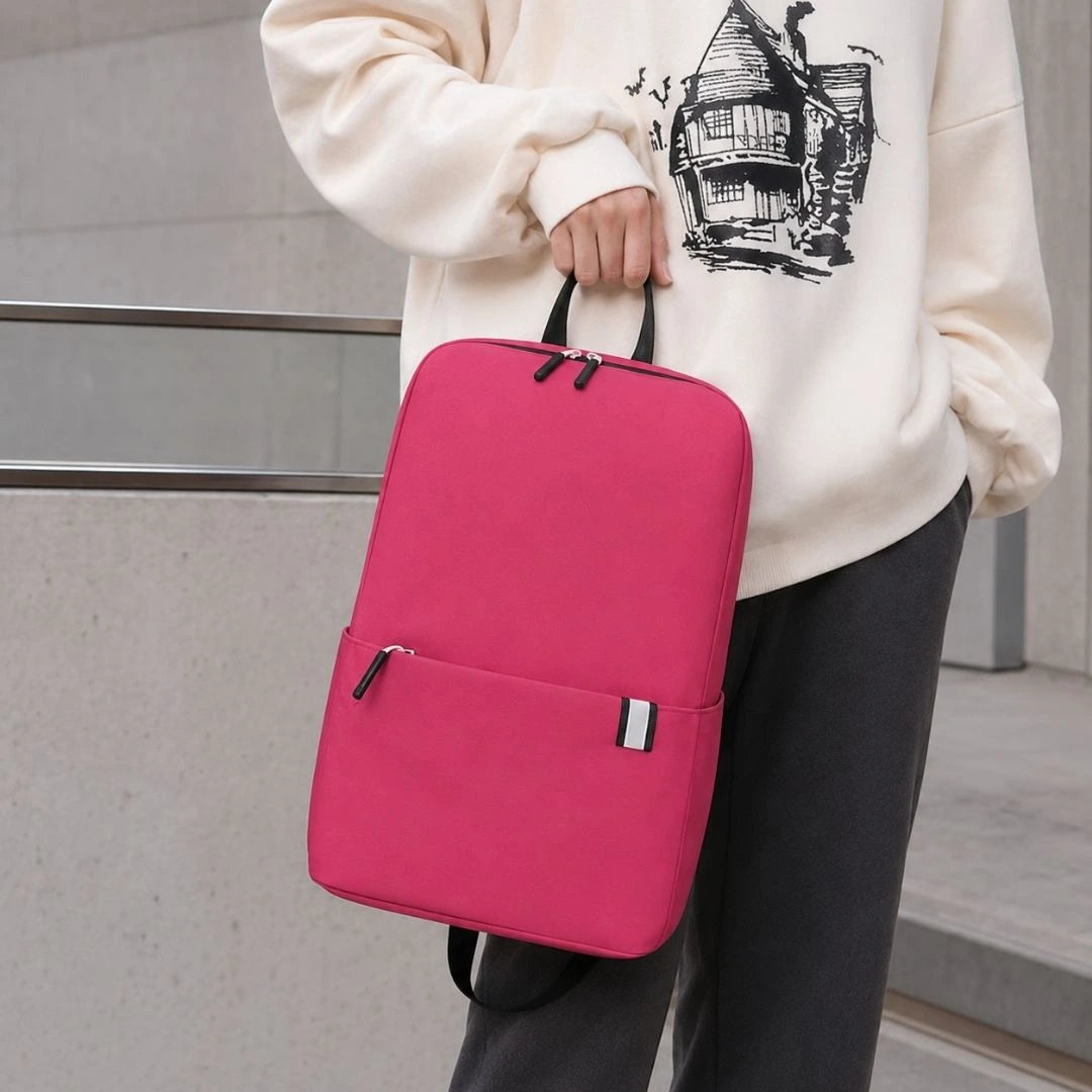 A person wearing a cream sweatshirt and dark gray pants carries a bright pink backpack with a top handle and a front zip pocket.
