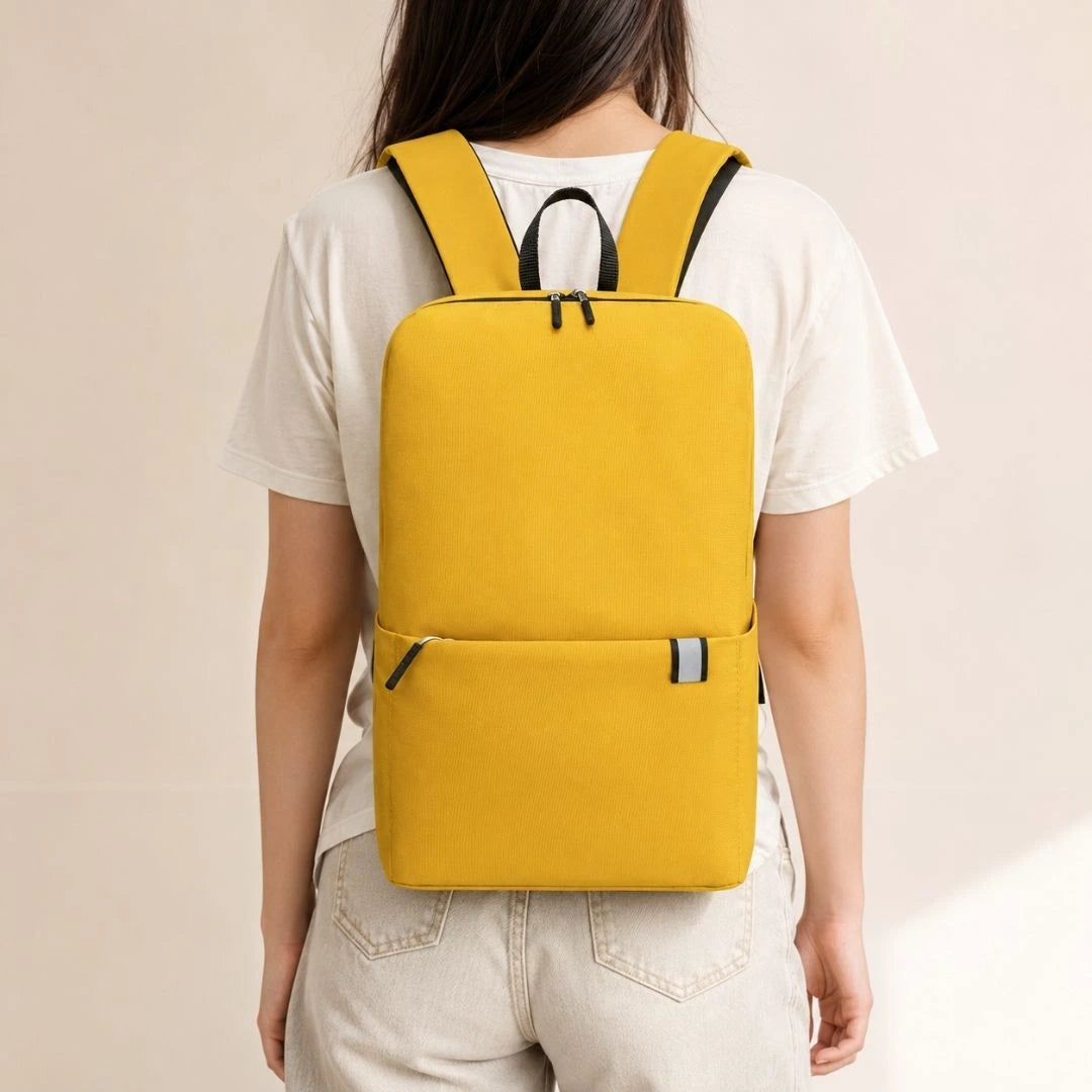 A person viewed from behind wearing a bright yellow backpack with black straps and zipper pulls over a white T-shirt and light pants.
