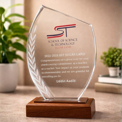 Glass award with wooden base on a surface, featuring text and logos.